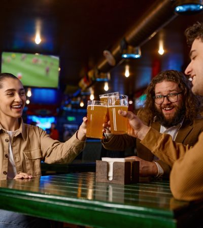 Friends watching football match clinking beer mug rest in sport bar